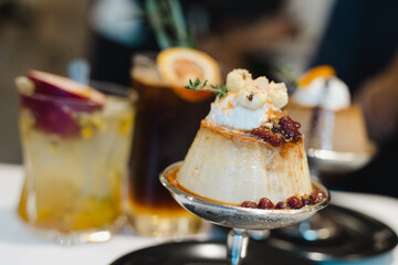 Pudding cake with rosemary, cream and red beans on sliver cup	, a few cocktail drink in the background on table