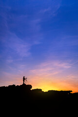Silhouette of a man photographer standing on top of mountain at sunrise background. The photographer raised hands with the tripod takes photos high in the mountains. - obrazy, fototapety, plakaty