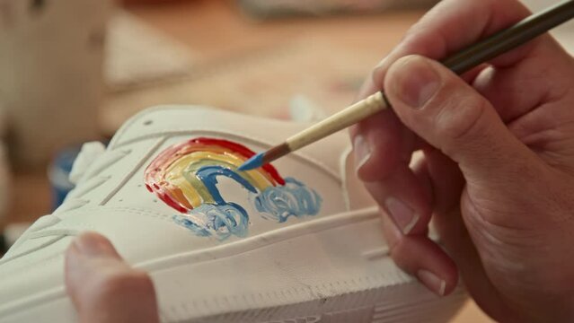 Extreme close up of unrecognizable person drawing rainbow on white sneaker indoor at daytime