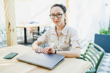 Happy woman sitting at outdoor cafe table and talking on phone with cup of coffee, smiling woman enjoying telecommuting in cafe or studying online