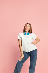 Portrait of young beautiful girl in casual clothes and headphones against pink studio background. Dreamy thoughtful face