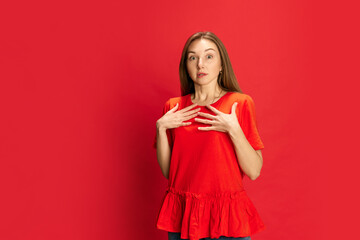Portrait of young beautiful woman standing with shocked face against red studio background. unexpected news, surprised