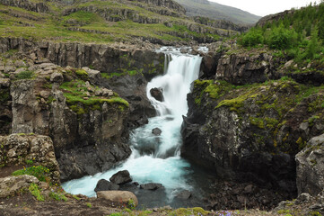 Scenic view of a waterfall flowing between grass cliffs