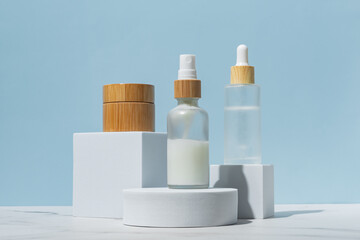 Set of beauty products in glass and bamboo bottles on white podiums on blue background. Skin care...