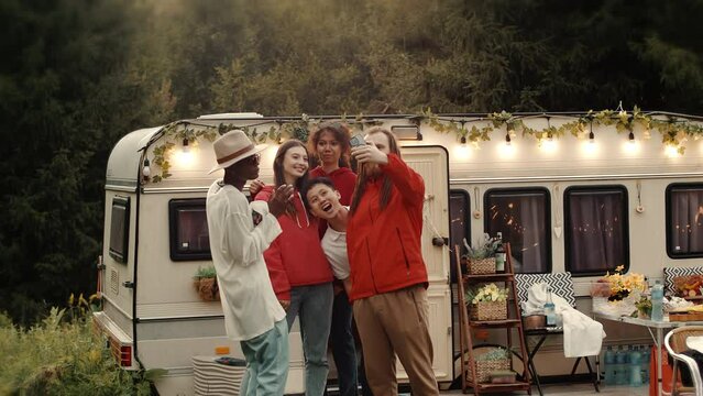 International Group of friends dancing at outdoor party relaxing together enjoy music. Boho chic decorated wan on a background. Smiling and posing on a camera, doing selfie
