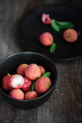 Fresh ripe lychee fruit and peeled lychee with green leaves on wooden background. Rustic style