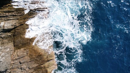 The dynamic power of a foamy blue wave crashing against rugged sea rocks The vibrant blue hue and the white foam create a visually striking image that portrays the raw energy and beauty of the sea