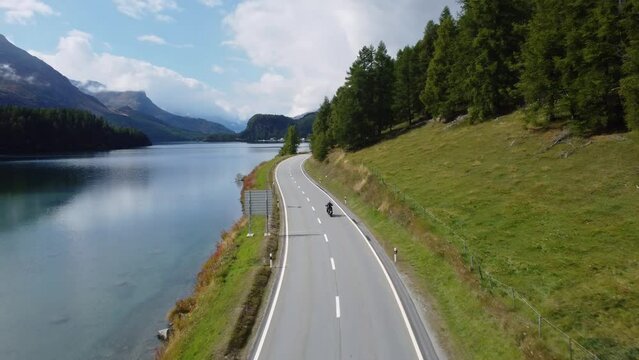 Sils Maria, Switzerland: Aerial drone footage following a motorcycle riding on the road along lake Sils in the Engadin valley near St Moritz in Canton Graubunden in the Swiss alps in late summer. 