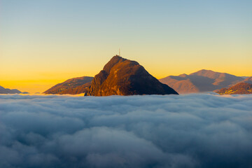 Mountain Peak San Salvatore Above Cloudscape with Sunlight and Clear Sky in Lugano, Ticino in...