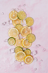 lemon and lime slices and ice on pink marble background
