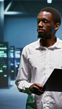 Vertical video African american engineer doing maintenance in data center providing vast computing resources and storage, enabling artificial intelligence to process massive datasets for training and