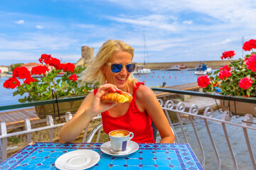 woman in a red dress, savors a delightful breakfast of croissant and cappuccino at an Italian cafe....