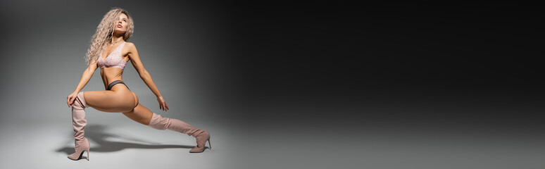 full length of fashion-forward and sexy woman in lace lingerie and long boots standing in expressive pose on black and grey background, toned body, wavy ash blonde hair, banner with copy space © LIGHTFIELD STUDIOS