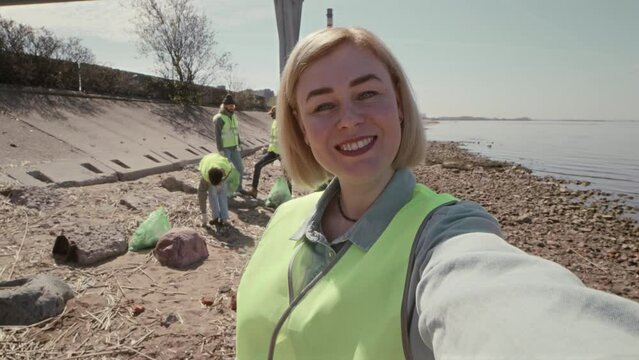 POV shot of female environmental volunteer looking at camera and speaking while filming vlog or video calling during shoreline cleanup