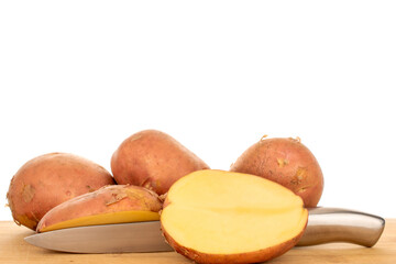 Several whole pink, raw potatoes and halves with a metal knife on a wooden kitchen board, macro, isolated on white background.