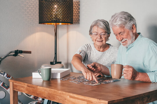 Carefree senior couple at home spend time together doing a puzzle on the wooden table. Elderly man and woman enjoying free time in retirement