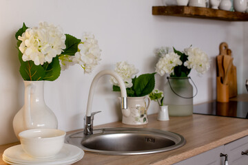 Wooden kitchen with floral decor. Cozy home decor. Kitchen utensils, dishes and a plate on the table. kitchen table in the dining room. Stylish kitchen with flowers in a vase.