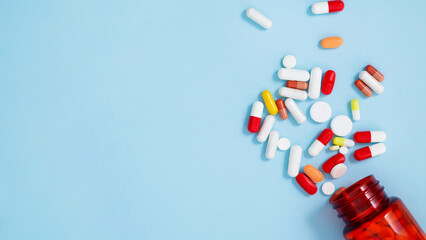 Orange bottle container with various colorful medication tablets and capsules on blue background. Concept of healthcare and medicine. Top view, copy space
