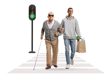 Young african american man with grocery bags walking with an elderly blind man at a pedestrian...