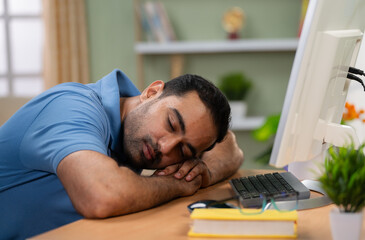 Fototapeta premium Tired Indian man sleeping on computer table at home - concept of resting, Stress relief and Overworked professional
