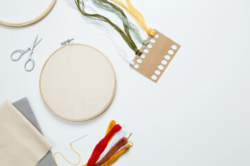 Embroidery set fot stitching. Beige cotton cloth in embroidery hoop on white background with fabric, colorful threads, scissors and needls. Indoor hobby concept with copy space, top view © matucha12
