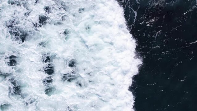 Wide white front of crashing wave glides quickly across surface of ocean, turning dark water into bubbling mixture of foam and seawater. It then darkens and transforms into beautiful texture