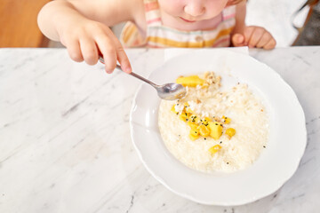 Little kid having breakfast at cafe. Adorable girl drinking still water, eating rice porridge with mango. enjoying breakfast. 