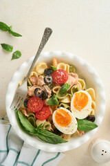 Italian pasta salad. Orecchiette pasta with tuna, tomato cherry, olive, basil and parmesan cheese in plate on grey stone or concrete background. Traditional Italian cuisine. Flat lay. Copy space.