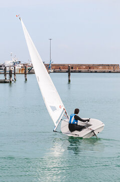 Back view, medium distance of, a single, male, controlling rutter of, one person sailing boat,,moving to race, start location