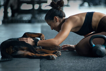 Fitness girl teasing and playing with her dog in the fitness gym, relationship between owner and pet