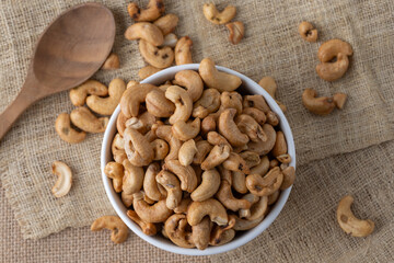 Roasted cashew nuts and halves in wooden bowl on table top view. Macro studio shot Homemade Roasted Salted Cashews in basket and spoon breakfast on sack, Healthy food Seeds snack product