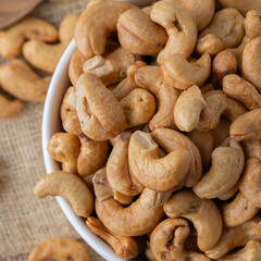 Roasted cashew nuts and halves in wooden bowl on table top view. Macro studio shot Homemade Roasted Salted Cashews in basket and spoon breakfast on sack, Healthy food Seeds snack product