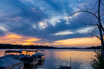 A beautiful sunset on a lake with a pier, pontoon boats, and a dead tree.