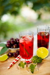 Fototapeta na wymiar Cherry lemonade with ice and lime in glasses. Summertime cool drink.