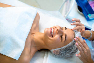 Fototapeta premium Cosmetologist preparing client for cosmetic procedures by putting disposable cap on woman head