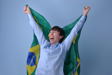 homem brasileiro feliz celebrando vit&oacute;ria do brasil com bandeira brasileira em fundo azul 