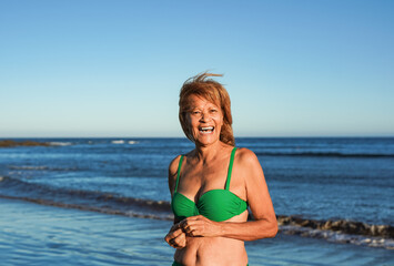 Obraz premium Happy senior latin woman smiling on camera during summer vacation on the beach