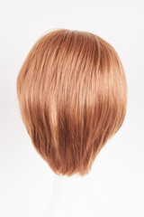 Natural looking ginger wig on white mannequin head. Short hair on the plastic wig holder isolated on white background, back view.
