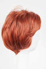 Natural looking ginger wig on white mannequin head. Short hair on the plastic wig holder isolated on white background, side view.