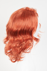 Obraz premium Natural looking ginger wig on white mannequin head. Medium length hair with wavy curls on the plastic wig holder isolated on white background, side view