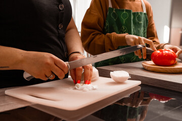 close-up detail of hands A mom wearing an apron and chopping an onion and her brown-haired 10-year-old son chopping a tomato - they are in a sunny kitchen-Pictures of family cooking-