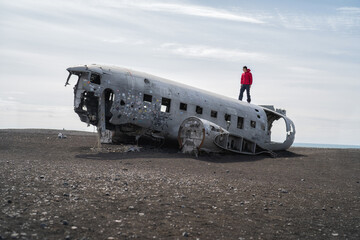 A tourist man standing on the wrecked plane or airplane in Iceland. Landmark