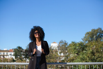 Young beautiful black woman with afro hair dressed in casual clothes is in seville, spain. The woman is happy and smiling. In the background the river and part of the city. Travel and holiday concept.