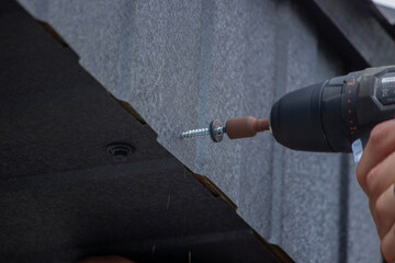 a man repairs the roof, tightens the self-tapping screw with a screwdriver.