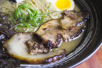Close-up photo of Japanese pork miso ramen consisting of broth, miso, pork, sliced scallions, sliced mushrooms, soft half boiled egg or ajitsuko tamago ajitama in a bowl on a wooden table.