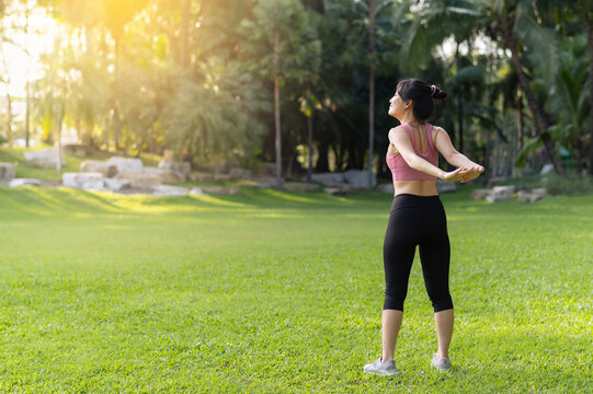 Female jogger. Get inspired fit active image of Asian young woman in pink sportswear stretching muscles in park before run, enjoying healthy outdoor activity. Wellness and fitness in natural setting.
