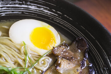 Close-up photo of Japanese pork miso ramen consisting of broth, miso, pork, sliced scallions, sliced mushrooms, soft half boiled egg or ajitsuko tamago ajitama in a bowl on a wooden table.