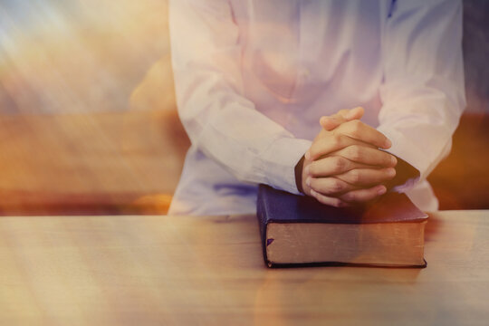 Close up of a woman hands praying to God on the bible on wooden table in dark room  with light from window. Christian background with Copy space.