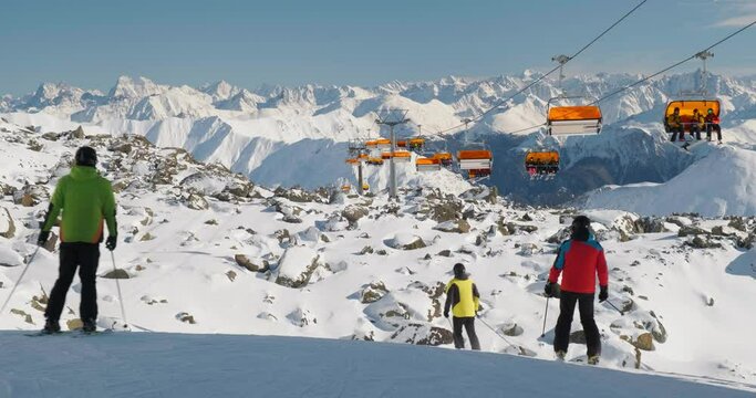 Orange chairlift and unrecognizable skiers in Samnaun - Ischgl - Paznaun ski resort, located in Austria and Switzerland. Winter, ski, chair lift.