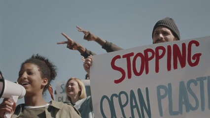 Group of young diverse environmental activists holding banner with Stopping ocean plastic sign and speaking in megaphone on protest against water pollution